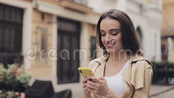 漂亮的年轻女孩用她的智能手机打字和微笑而不是站在老城的背景下看着前方视频的预览图