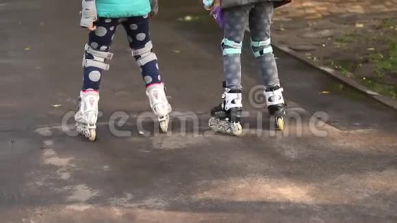 两个可爱的小白种人女孩在城市公园的雨后在潮湿的人行道上玩滑轮滑视频的预览图
