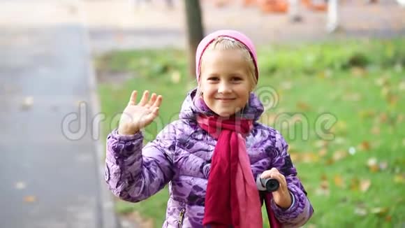 可爱可爱的白种人金发快乐的学校女孩微笑和挥手在城市公园温暖的秋天快乐的孩子视频的预览图