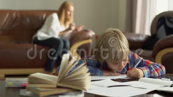 可爱的小男孩在家中的笔记本上写下上写下信息而他的母亲则坐在笔记本上视频的预览图