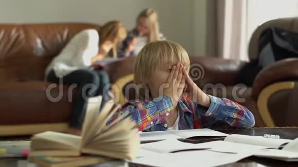 有趣的小男孩坐在桌子前笔记本在家里的前景妈妈和姐姐坐在视频的预览图
