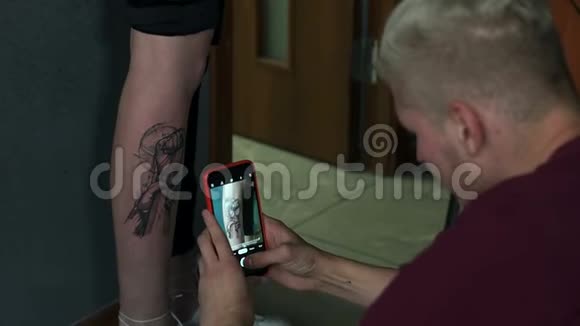 纹身师在手机上拍照一个女孩腿上的新纹身视频的预览图