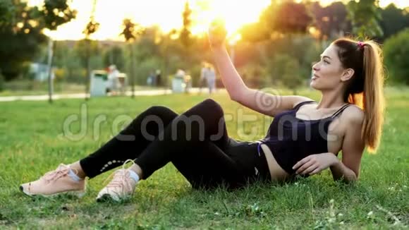 体育女博客写手在手机上为博客自拍日落时分躺在城市公园的草地上有一个视频的预览图