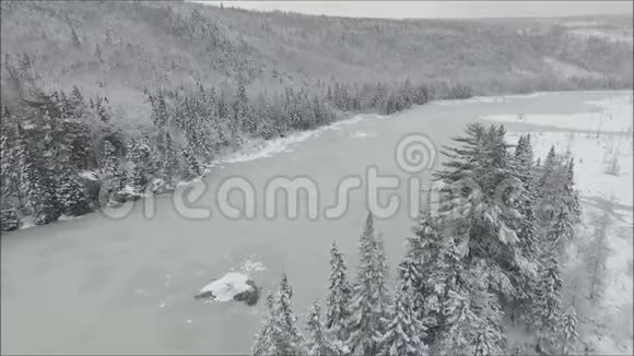 雄伟的空中无人机在白雪皑皑的冰雪覆盖的湖河上盘旋在寒冷的冬天山山景观中有松树视频的预览图