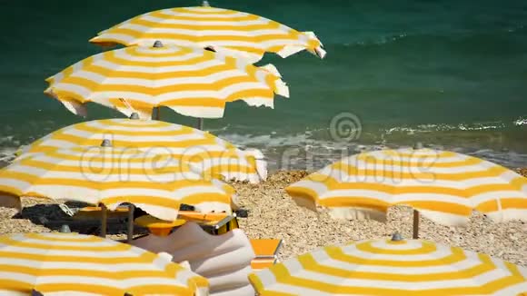 在一个有风的夏天黄色和白色条纹的雨伞在布满卵石的海滩上打开视频的预览图