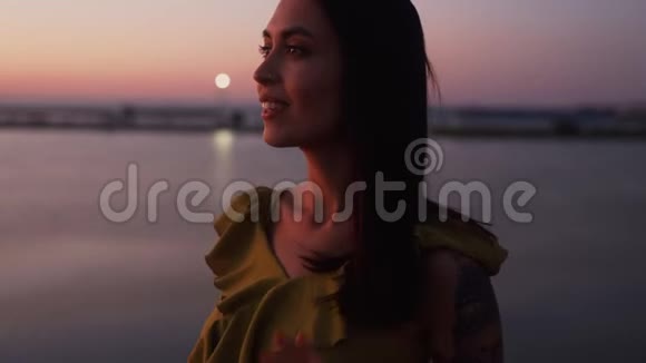 日落时微笑的女人的肖像背景风吹着她的头发视频的预览图