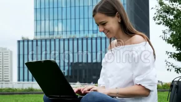 年轻女性坐在草地上使用笔记本电脑女商人用键盘打字现代商业的特写肖像视频的预览图