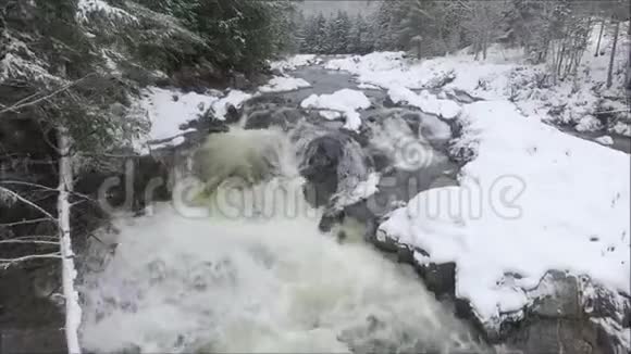 空中无人驾驶飞机在蜿蜒的森林雪山景观中的岩石上飞过冷水流视频的预览图