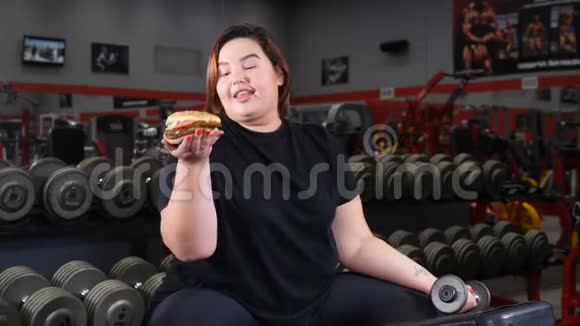 意志力和减肥理念肥胖的漂亮女人在健身房锻炼时休息吃零食女孩视频的预览图