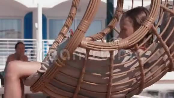在度假酒店放松的少女躺在挂椅上带着智能手机穿着比基尼的少女视频的预览图