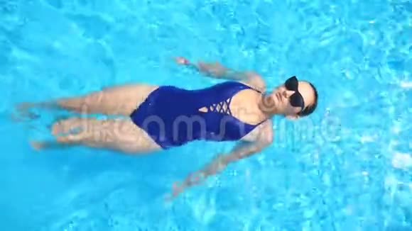 女人带着清澈的水在游泳池后面游泳优雅的女孩戴太阳镜在热带度假胜地放松视频的预览图