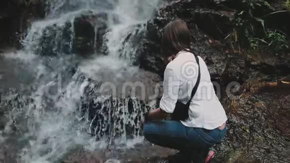 女徒步旅行者蹲伏在飞溅的丛林瀑布中视频的预览图