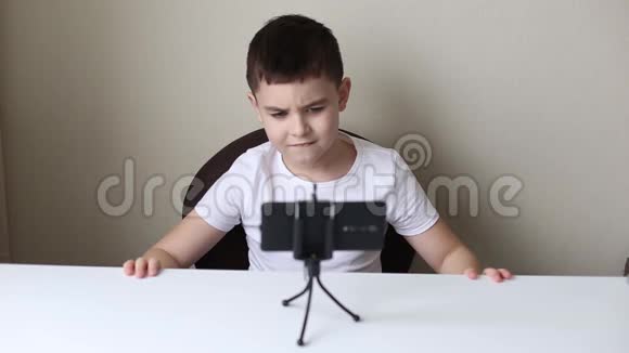 一个棕色头发的男孩坐在白色桌子旁看着一部智能手机视频的预览图