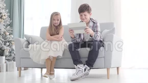 害羞的白种人漂亮的女孩坐在男孩旁边手里拿着平板电脑布鲁内特那家伙无视可爱的孩子视频的预览图