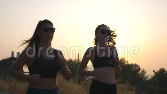 两个运动的女人沿着乡村道路慢跑背景是日落晚上在户外工作的年轻女孩视频的预览图