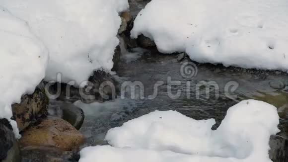 近景拍摄的冰川水溪几乎没有穿过覆盖着雪的岩石视频的预览图