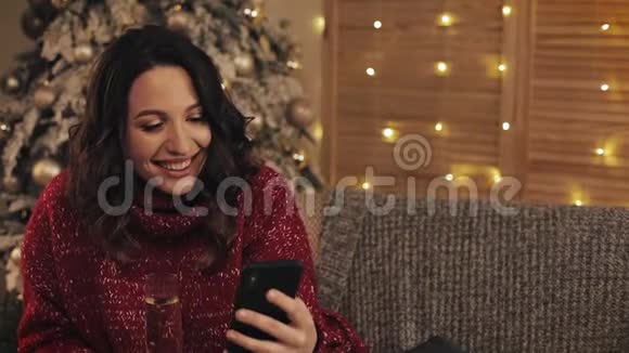 迷人的布鲁内特女士看着她的智能手机屏幕笑着拿着一杯香槟坐在科西视频的预览图