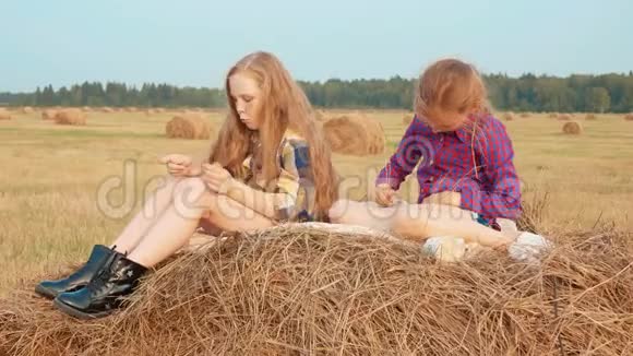 两个十几岁的女孩在乡间的收割场上的干草堆上放松少女和少年正在睡干草视频的预览图