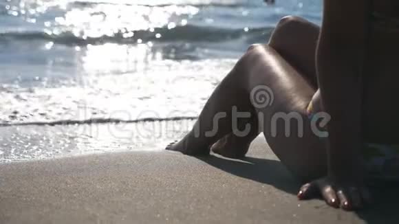 一个双腿修长的年轻女孩坐在热带海滩上伴着浪花嬉戏享受着假期在海边放松的女人视频的预览图