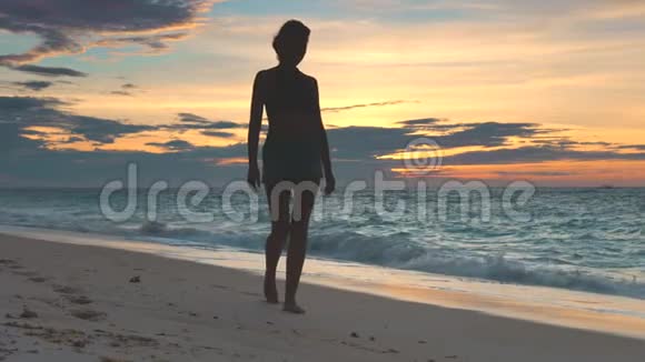 女人在美丽的夕阳下沿着海岸线散步视频的预览图
