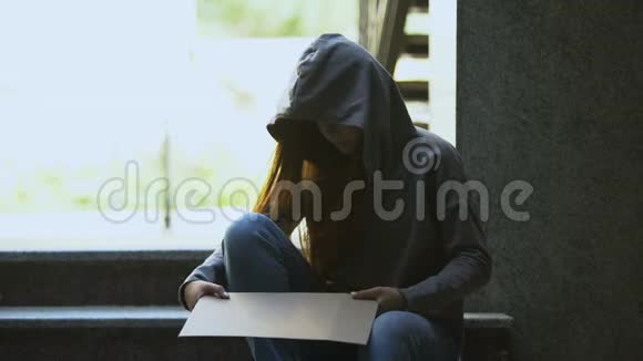 穿着连帽衫的无家可归少女在楼梯上显示帮助标志社会不安全视频的预览图