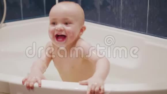 一个小男孩脸上挂着肥皂泡站在浴缸里在镜头后面和妈妈开心地笑着视频的预览图