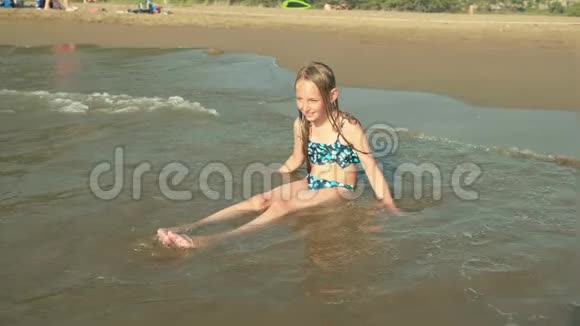穿泳装的可爱女孩坐在沙滩上享受海浪视频的预览图
