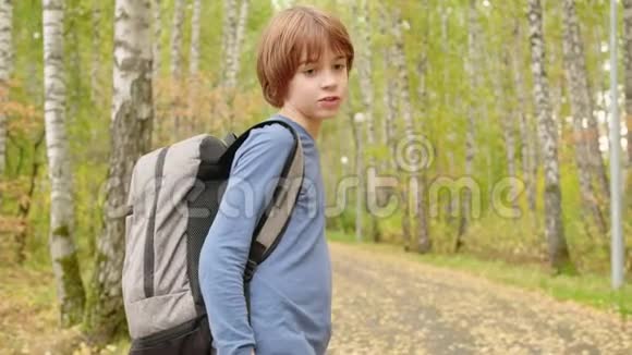 一个背着背包走在秋天公园小路上的少年男孩秋天在城市公园的路上看到少年杜松子酒视频的预览图