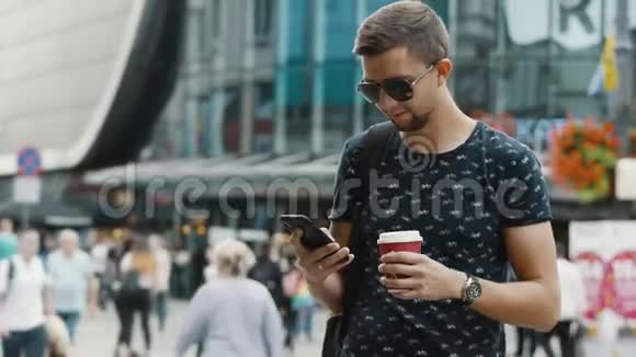 一个喝咖啡的现代男人在拥挤的城市街道上使用手机视频的预览图