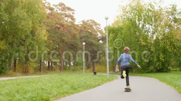 美丽的绿色公园里可爱的十几岁男孩骑滑板的后视镜视频的预览图