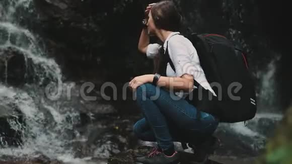 女旅行者蹲在飞溅瀑布附近视频的预览图