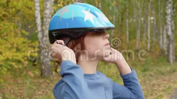 在秋天公园少年男孩把自行车头盔戴在头上穿蓝色防护头盔的帅哥视频的预览图