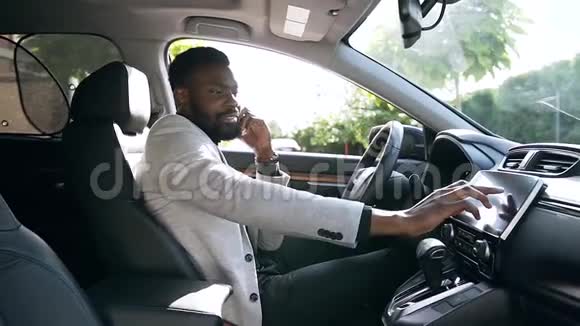 一位时尚活泼的非裔美国商人坐在司机座位上打着电话调着车视频的预览图