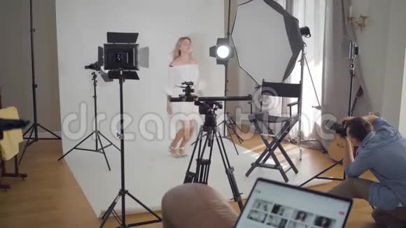 拍摄的后台专业摄影师拍摄年轻女性模特在白色背景下跳跃的照片视频的预览图
