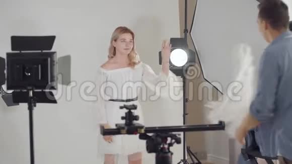 拍摄的后台摄影师在摄影棚里拍一张在白色背景上摆姿势的漂亮女孩的照片视频的预览图