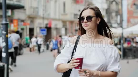 快乐的女游客拿着一杯咖啡站在拥挤的城市街道上散步等待一个男人约会人和人视频的预览图