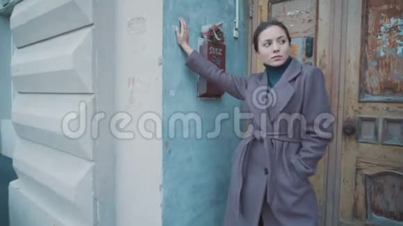 穿紫丁香外套的女孩站在老楼门口的街道上视频的预览图