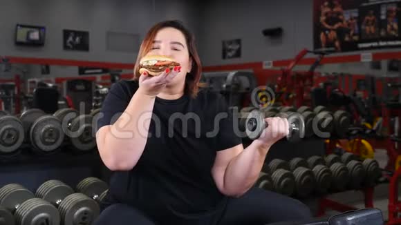 失去重量和意志力量的概念胖女人在健身房做运动女孩选择垃圾食品而不是视频的预览图