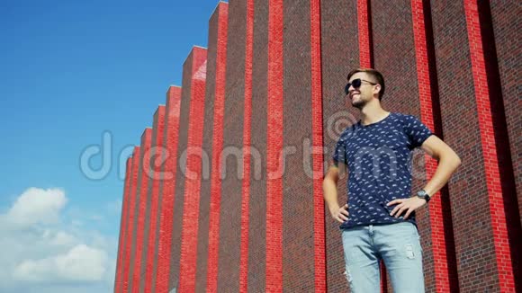 快乐男游客站在城市街道上戴着太阳镜靠近一座现代化的砖楼视频的预览图