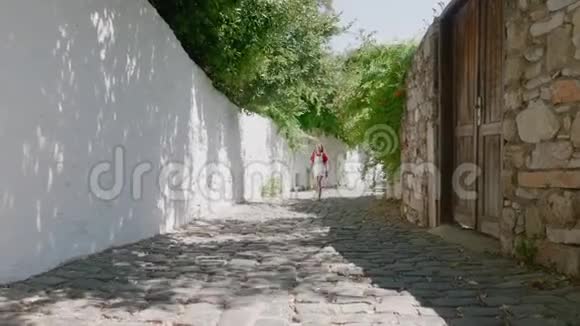 在旧城狭窄的街道上散步的女孩旅游女孩走在阳光明媚的街道上岩石墙背景夏天的老人视频的预览图