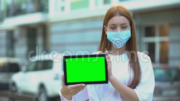 戴防护面罩的少女手持绿屏平板电脑预防流感小贴士视频的预览图