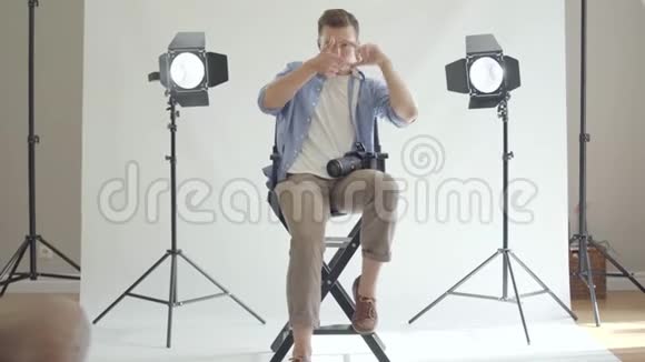专业的男摄影师坐在椅子上用手指注视着摄影棚里的摄像机视频的预览图