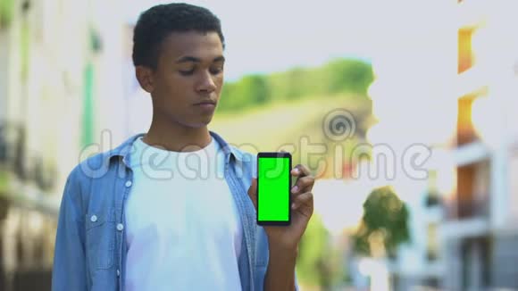 混血少年指着绿色屏幕智能手机游戏和信使视频的预览图