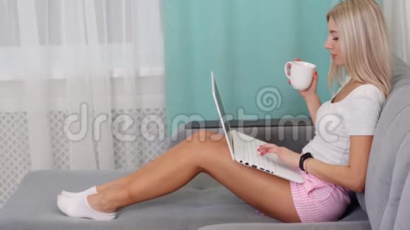 漂亮的女人坐在家里在网上工作或者通过笔记本上网购物喝咖啡概念启动视频的预览图