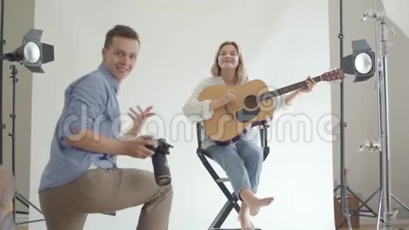 拍摄的后台专业有趣的摄影师拍摄年轻女孩一边弹吉他一边坐着的照片视频的预览图