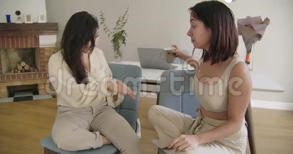 两个年轻的高加索女人坐在家里的软椅子上聊天漂亮的女孩欣赏她朋友的新指甲视频的预览图