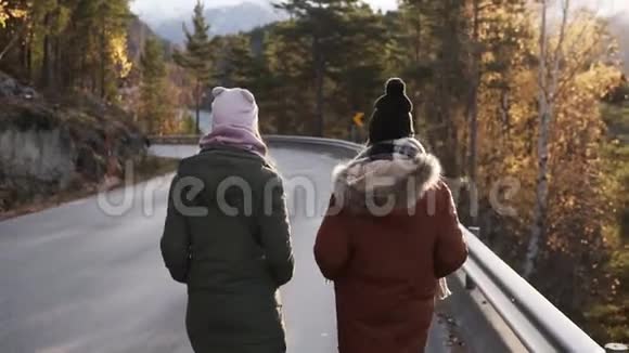 两名女游客在一条穿过乡村的长路上缓慢地走着走向雪山峰和视频的预览图