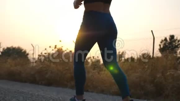 年轻健康女孩的脚在乡间小路上慢跑背景是日出苗条的女性腿在户外跑步体育运动视频的预览图