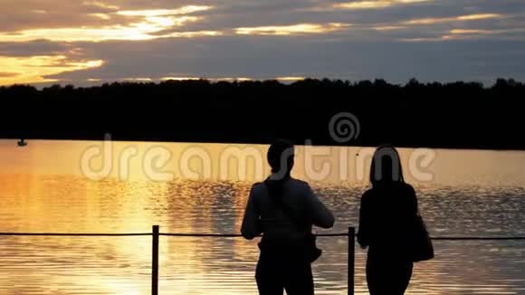 一位女游客的特写剪影两位女士在湖上的一座桥上欣赏傍晚的日落视频的预览图