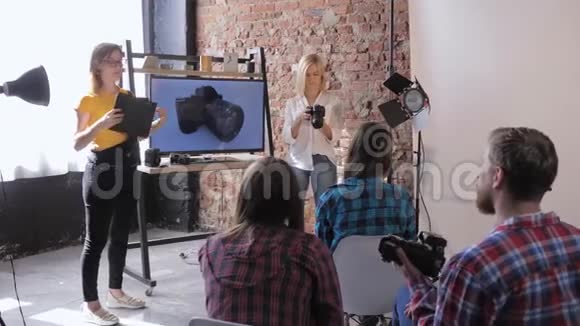 摄影学校时尚摄影师在电视背景下向现代摄影工作室的学生讲述相机设备视频的预览图